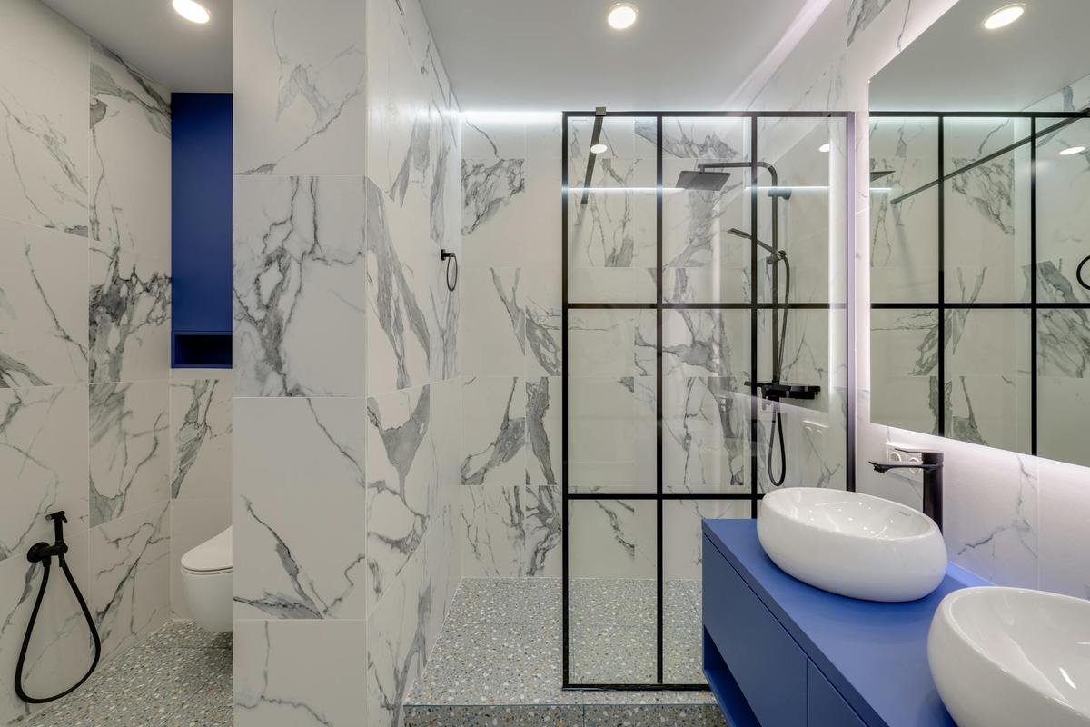 Modern bathroom with blue vanity, marble walls, and glass shower partition